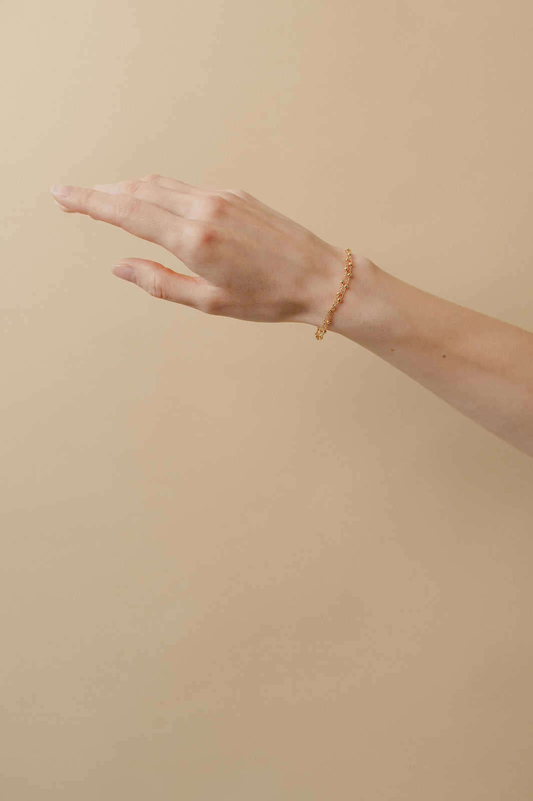 main d'une femme avec un bracelet en chaine bille doré sur un fond beige