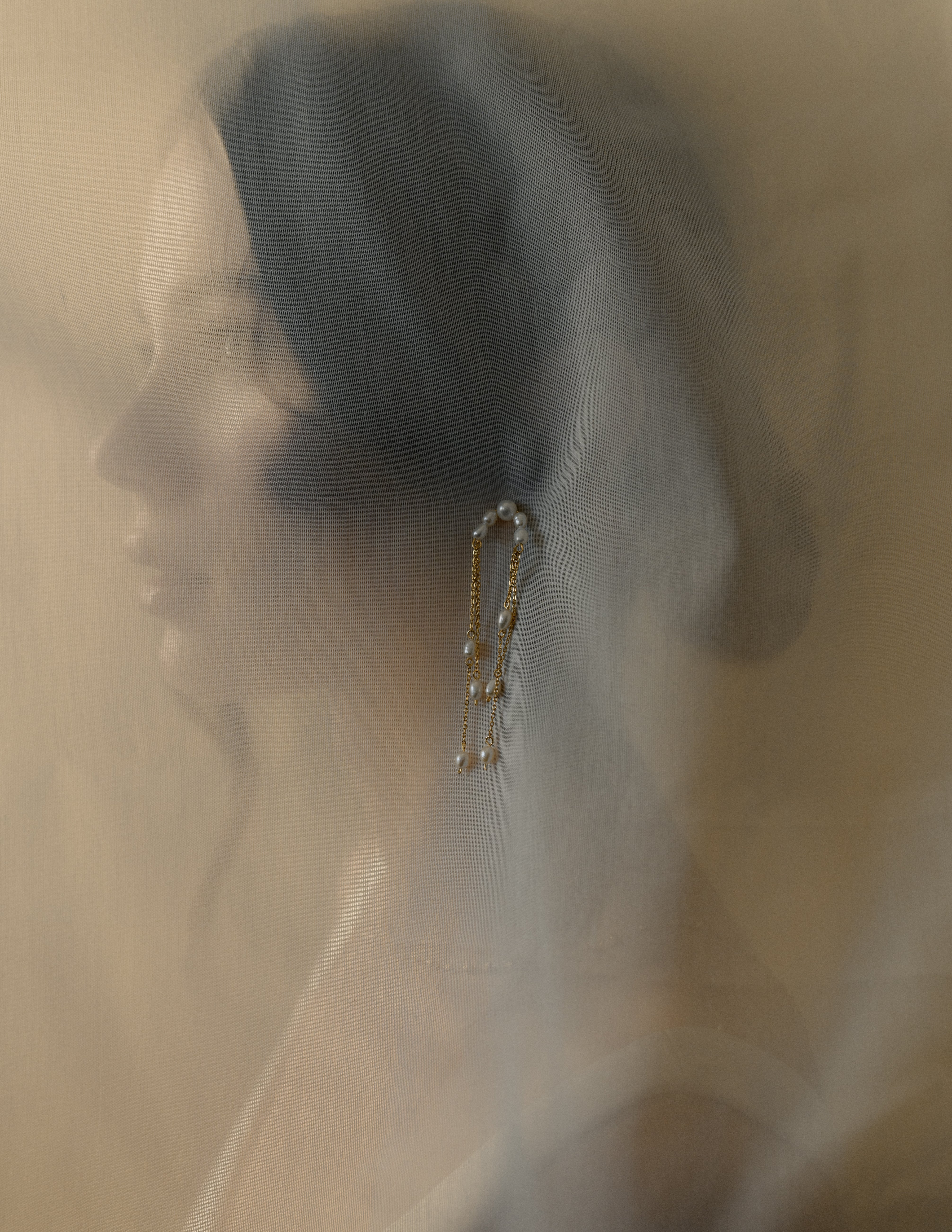 photo artistique du portrait d'une femme cachée par un voile de mariage et une boucle d'oreille posée sur le voile 