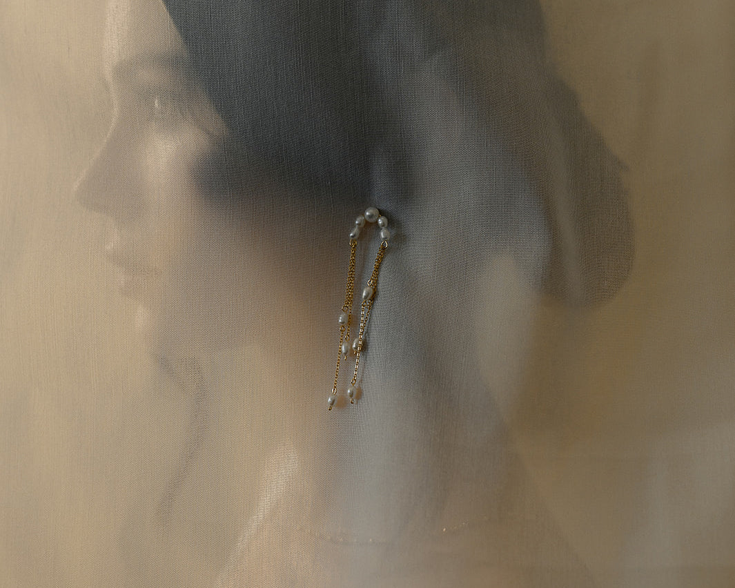 photo artistique d'une femme avec un chignon bas portant une boucle d'oreille sur un voile en tulle