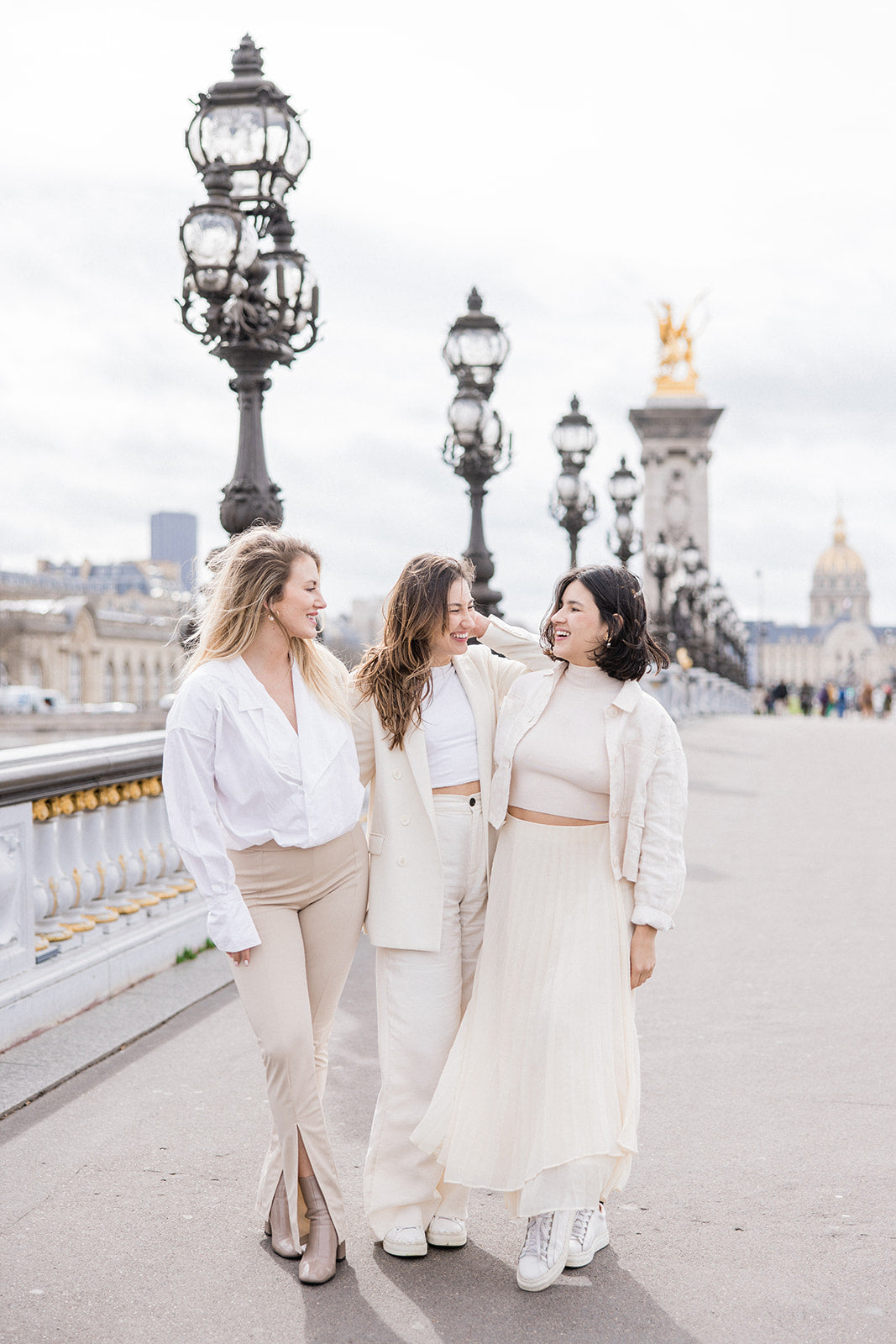 trois femmes entrain de sourire en se regardant sur un  ont mythique de la ville de Paris habillées en couleurs claires pour un mariage