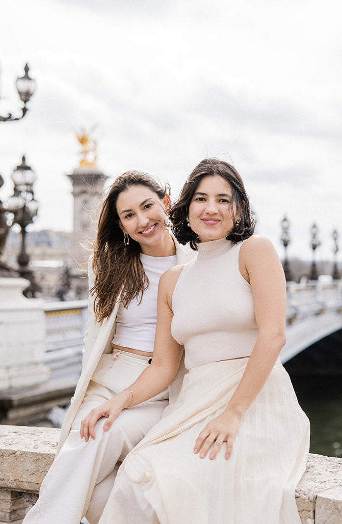 deux femmes accoudées sur un pont habillées en beige et souriant à la caméra