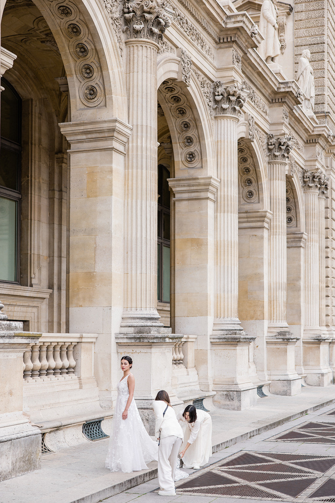 deux femmes en train d'arranger la traîne de la robe d'une mariée dans la ville de Paris