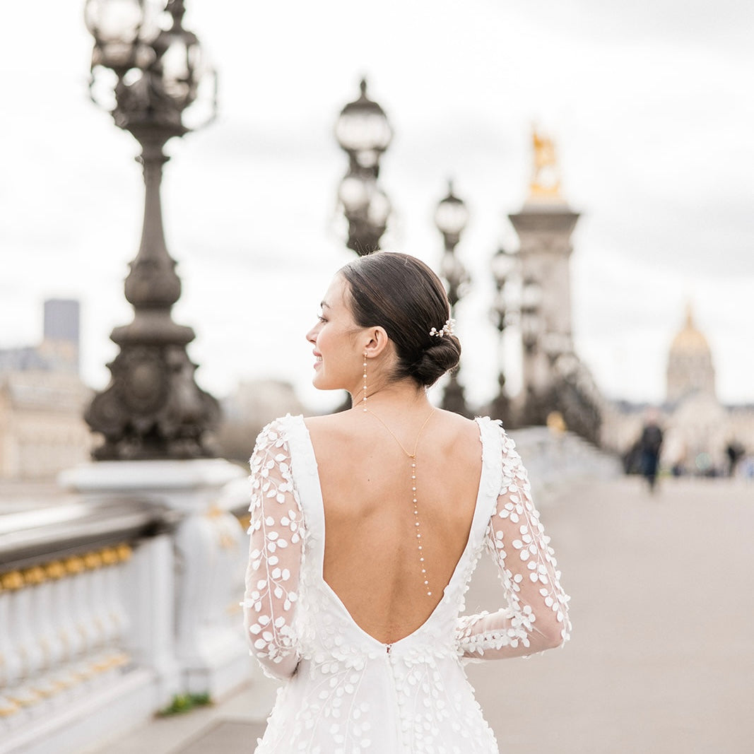 femme de dos sur un pont emblématique de la ville de Paris portant une robe de mariée avec des bijoux en perles naturelles pour un mariage