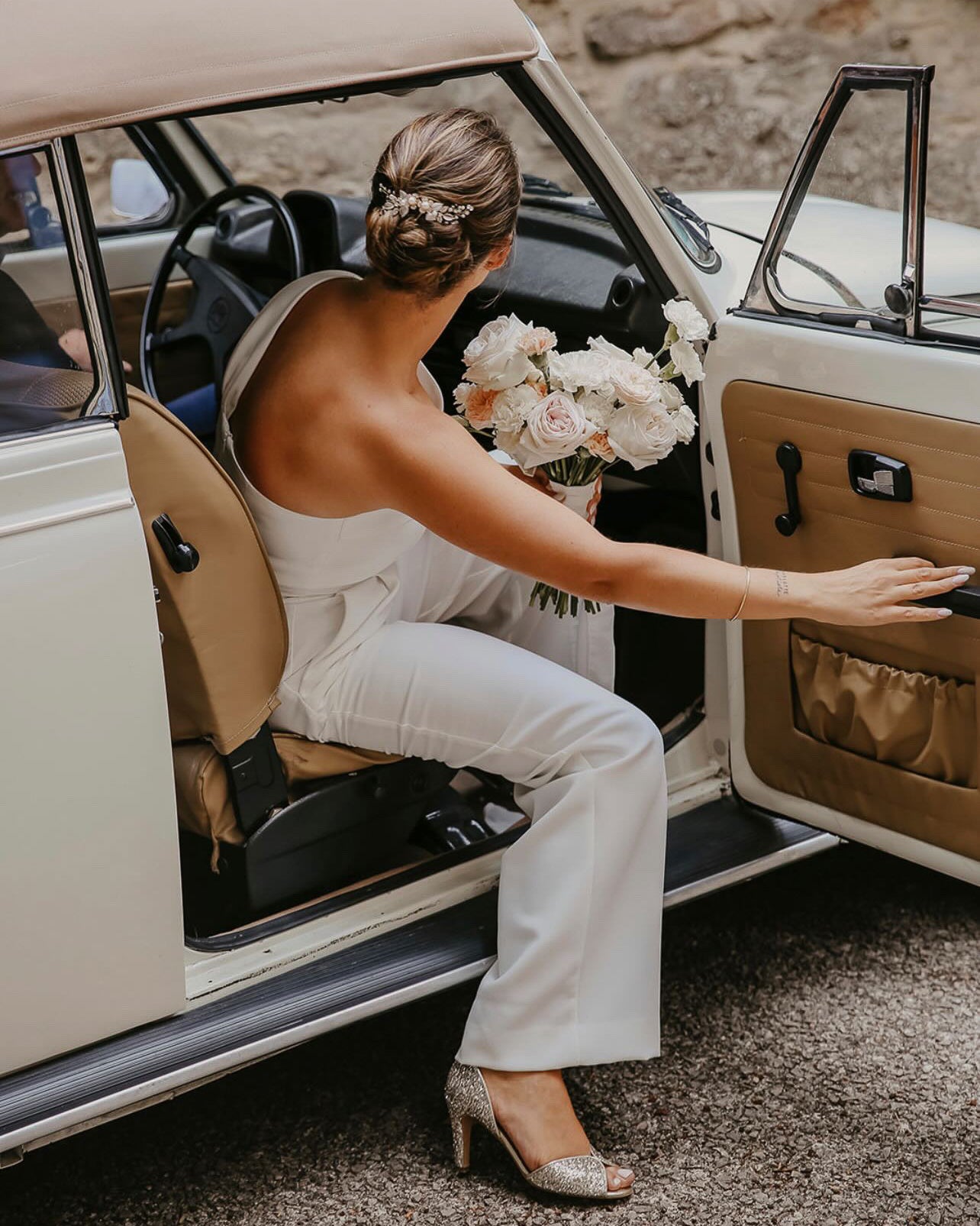 mariée sortant de la voiture pour son mariage civile portant une combinaison blanche son bouquet de fleurs et un chignon avec un peigne à cheveux