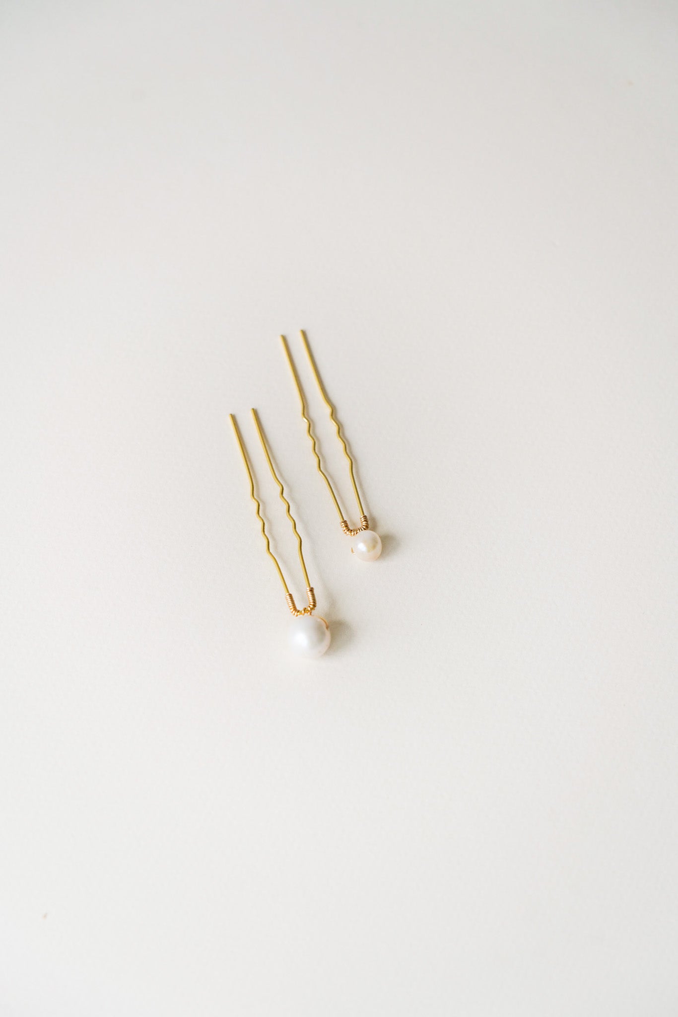 Pic délicat photographié sur fond blanc, orné de deux perles de culture blanches, une grande et une plus petite, soigneusement disposées côte à côte. La composition épurée met en valeur la brillance nacrée des perles, soulignant la finesse du travail artisanal. Un accessoire raffiné et intemporel, idéal pour sublimer une coiffure de mariée ou une tenue de cérémonie.