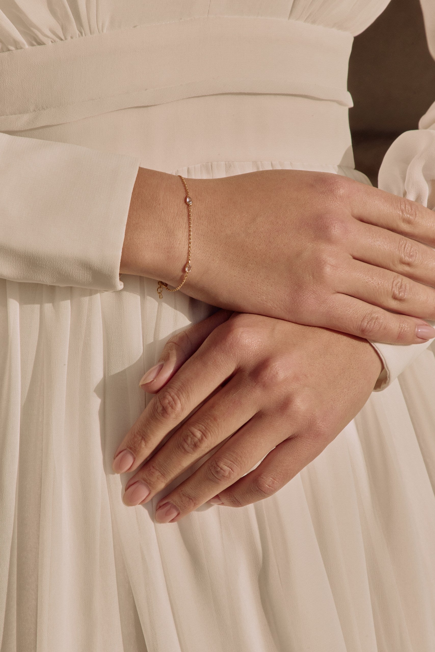 Gros plan de mains qui se croisent sur une robe de mariée mettant en avant le bracelet de mariage bleu