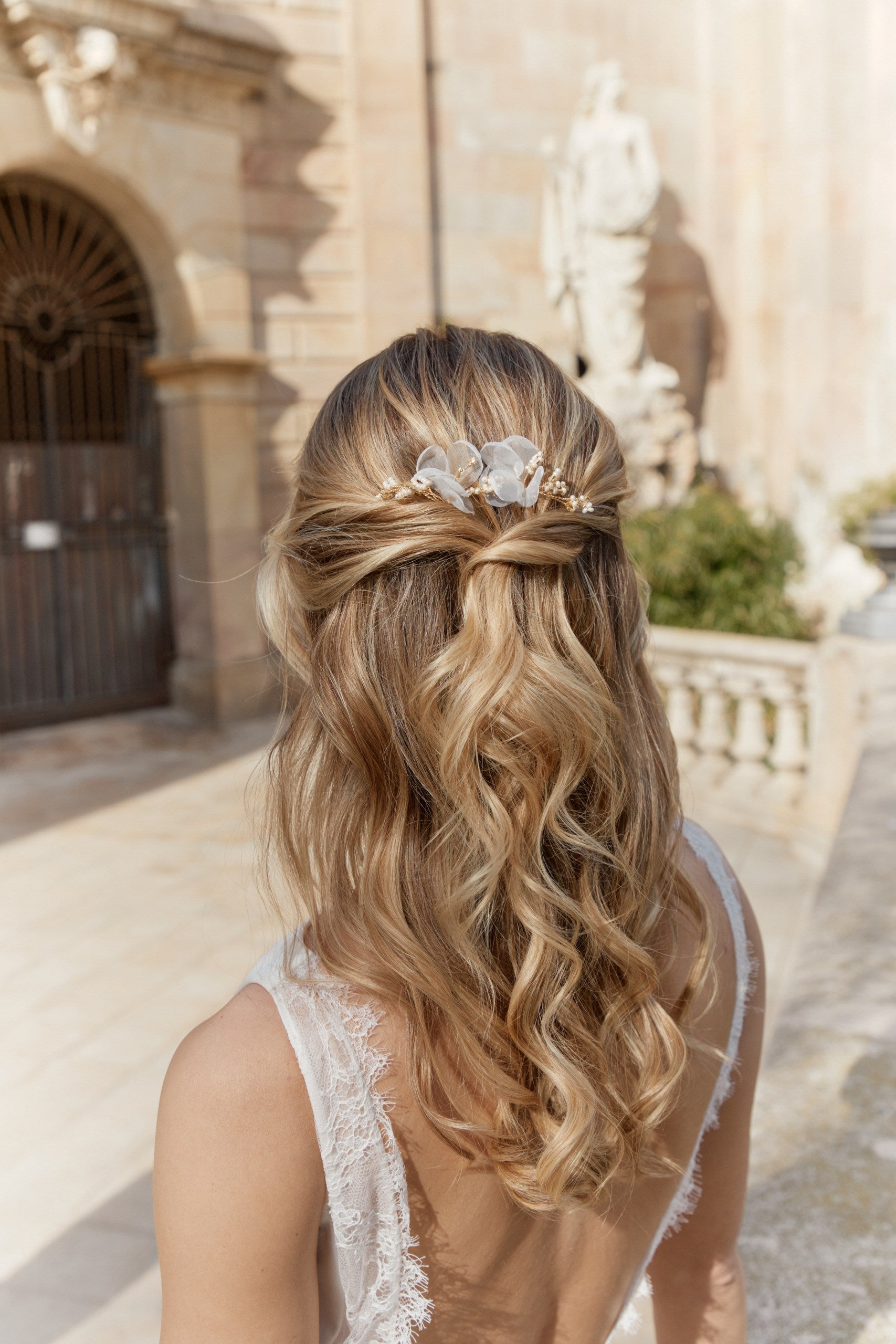 Jeune femme de dos montrant sa chevelure en demi queue de cheval de mariée ondulée accessoirisée par des pics en organza et perles rocailles 