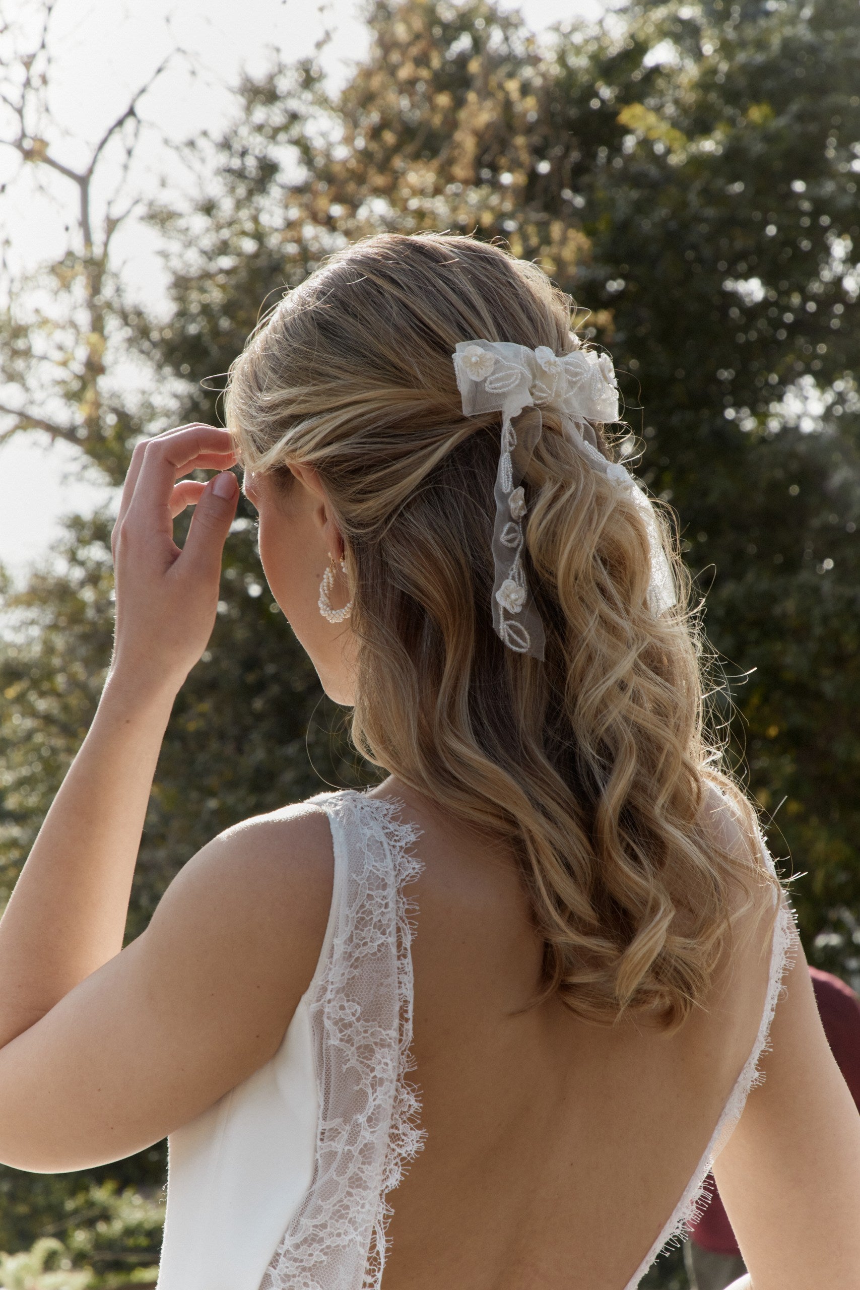 Femme de dos arborant une coiffure de mariée avec un noeud fleuri sur des cheveux lachées et ondulés