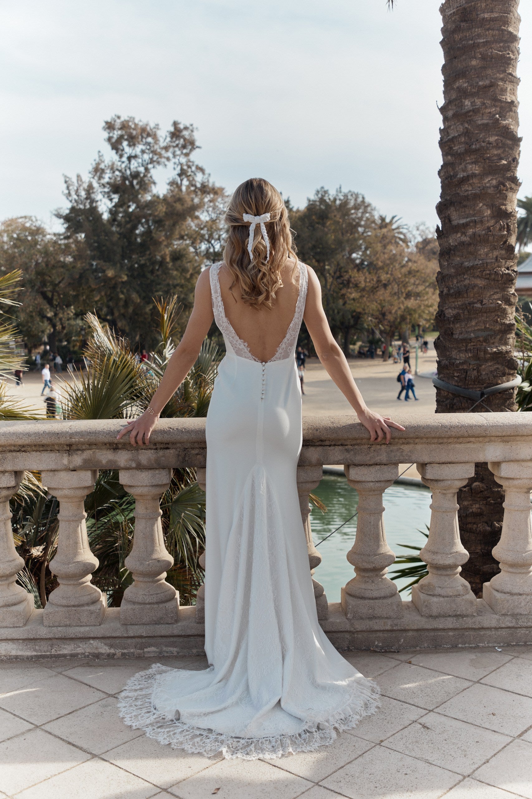 femme de dos posant les mains sur une estrade habillée en robe de mariée avec les cheveux détachés et un peigne de mariage en forme de noeud papillon