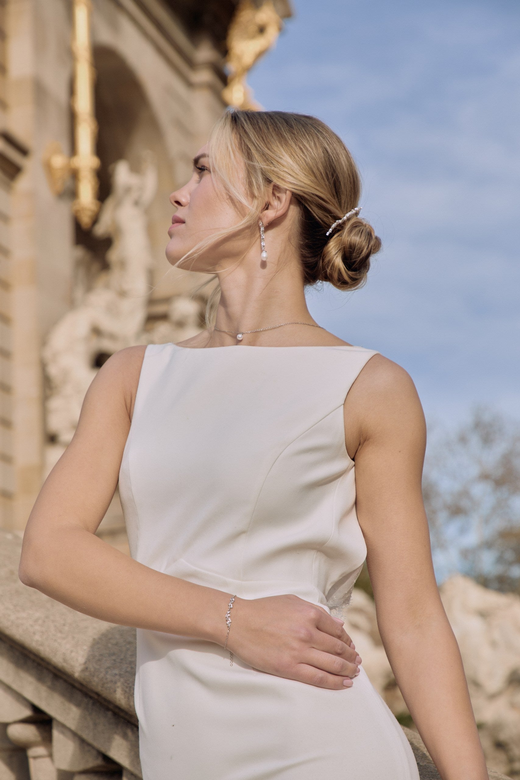 Jeune mariée qui regarde en l'air montrant son collier avec une perles et ses boucles d'oreilles