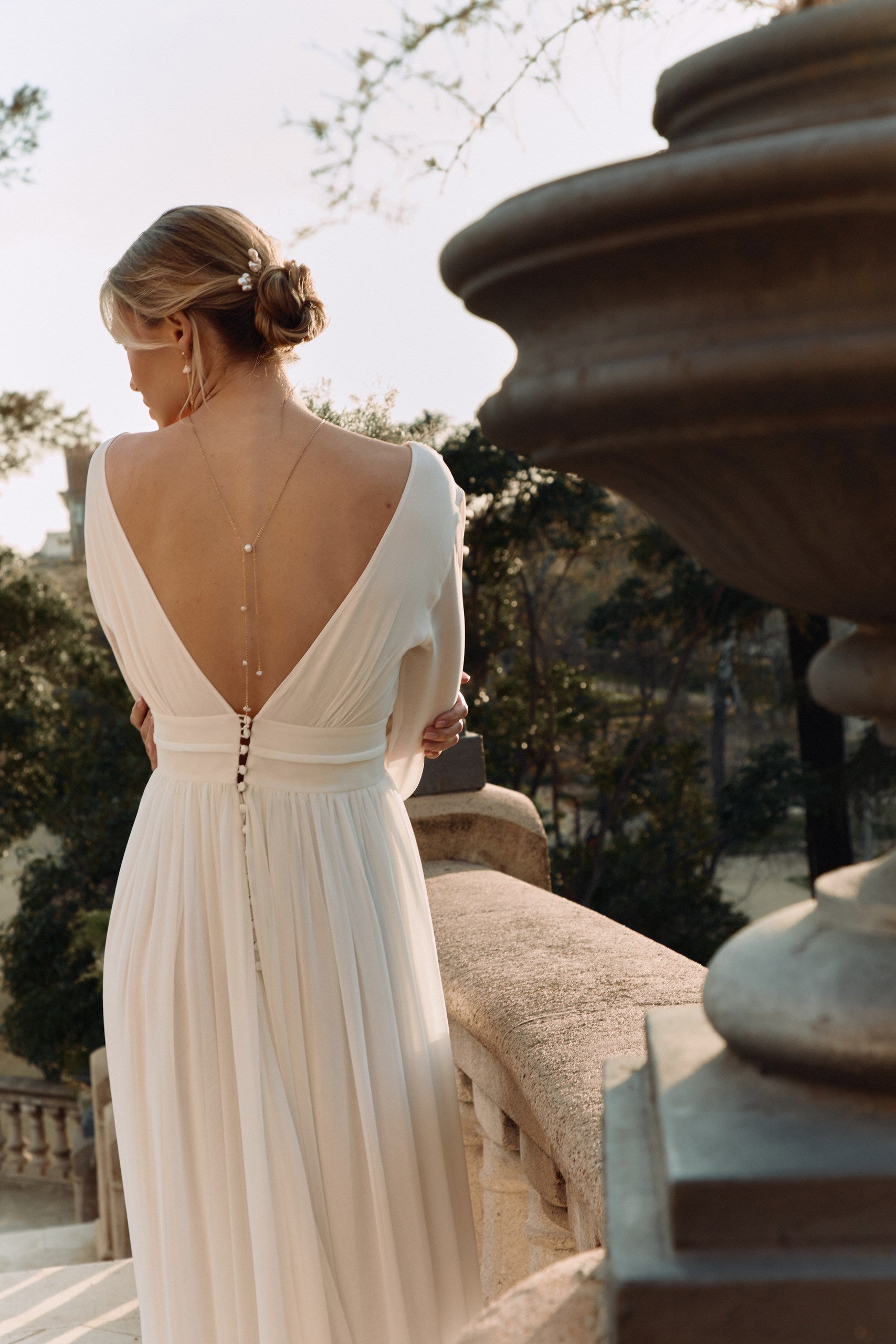Jeune femme en extérieur dans une robe romantique de dos montrant une parure de bijoux pour mariée