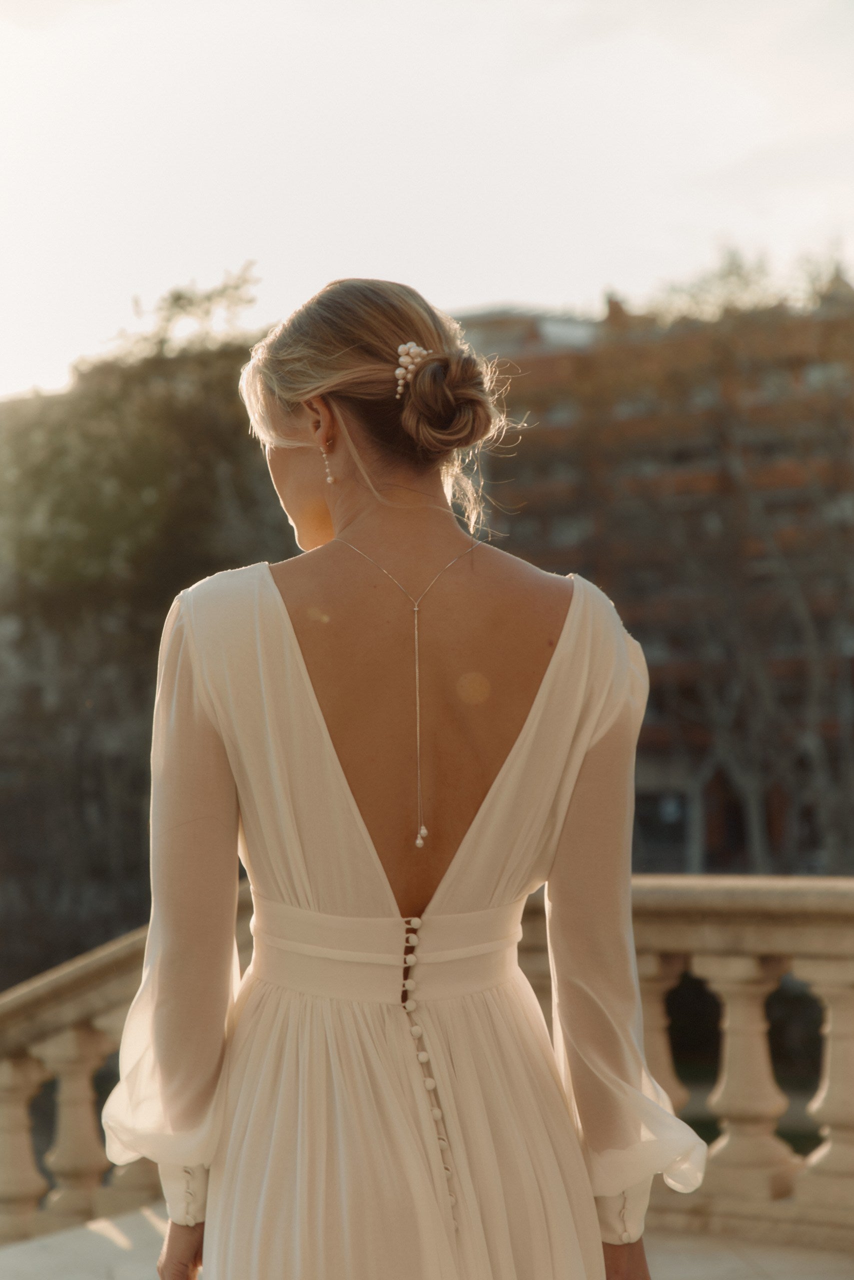 Femme de dos avec sa robe de mariée à grand décolleté de dos montrant son bijou de dos et son peigne qui est dans son chignon 