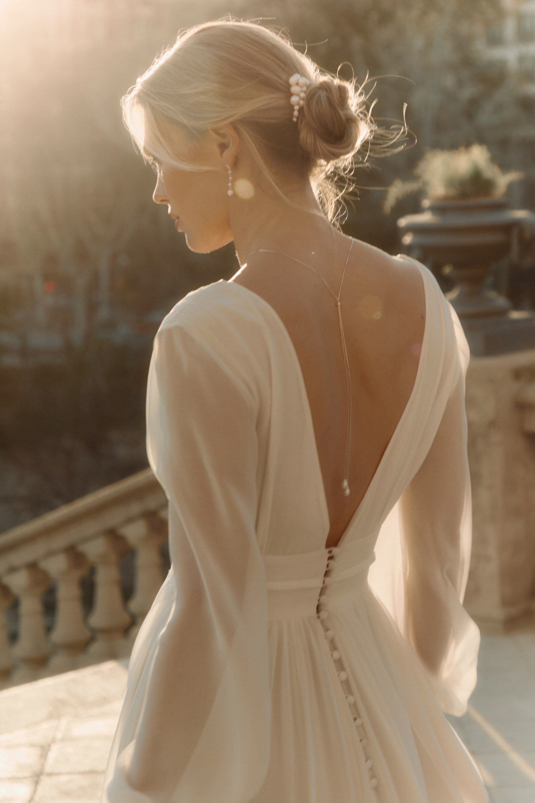 Femme de dos marchant avec sa robe de mariée avec un décolleté de dos qui montre une parure de bijoux luxe