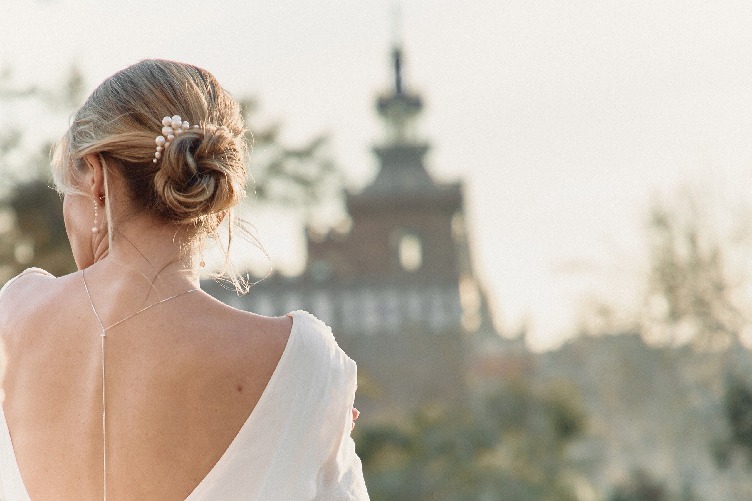 Jeune mariée de dos avec un chignon de mariage montrant son peigne en forme de nuage en perles naturelles