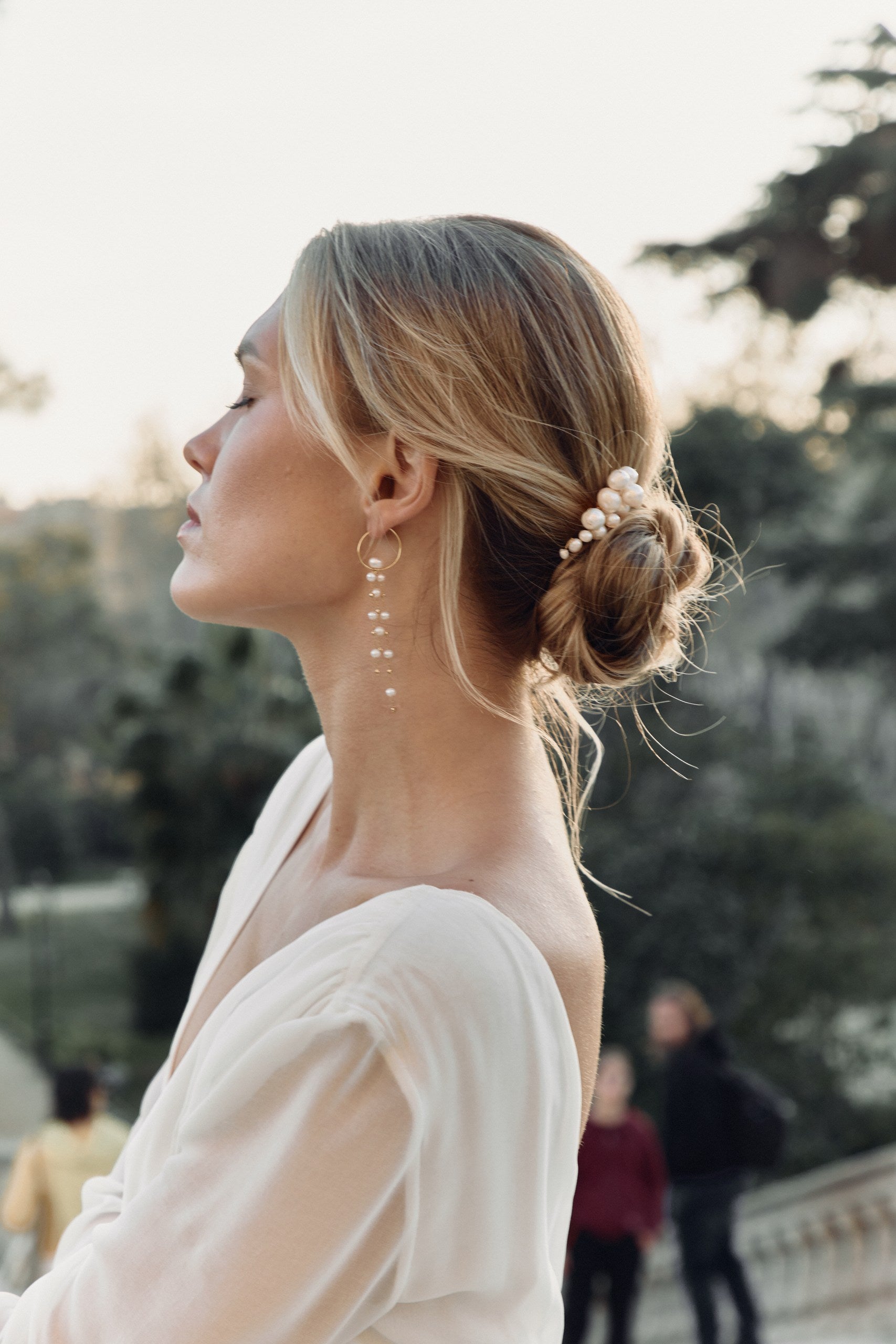 Femme de profil avec un chignon de mariage mettant en avant des boucles d'oreilles et un peigne 
