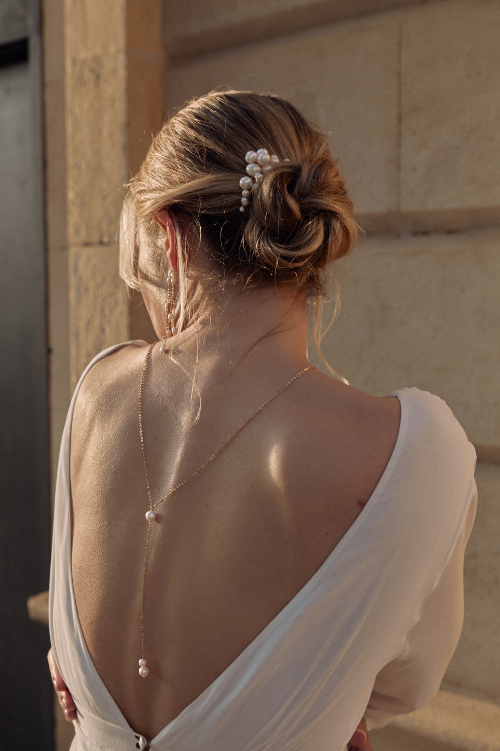 Jeune femme de dos montrant une robe à décolleter de dos avec un collier de dos minimaliste et un peigne en forme de nuage fait de perles naturelles