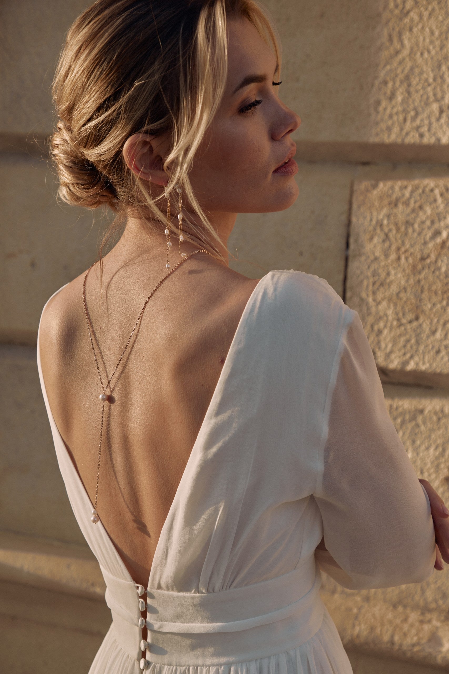 Jeune mariée portant une robe à décolleté de dos avec des bijoux en pierres naturelles raffinées