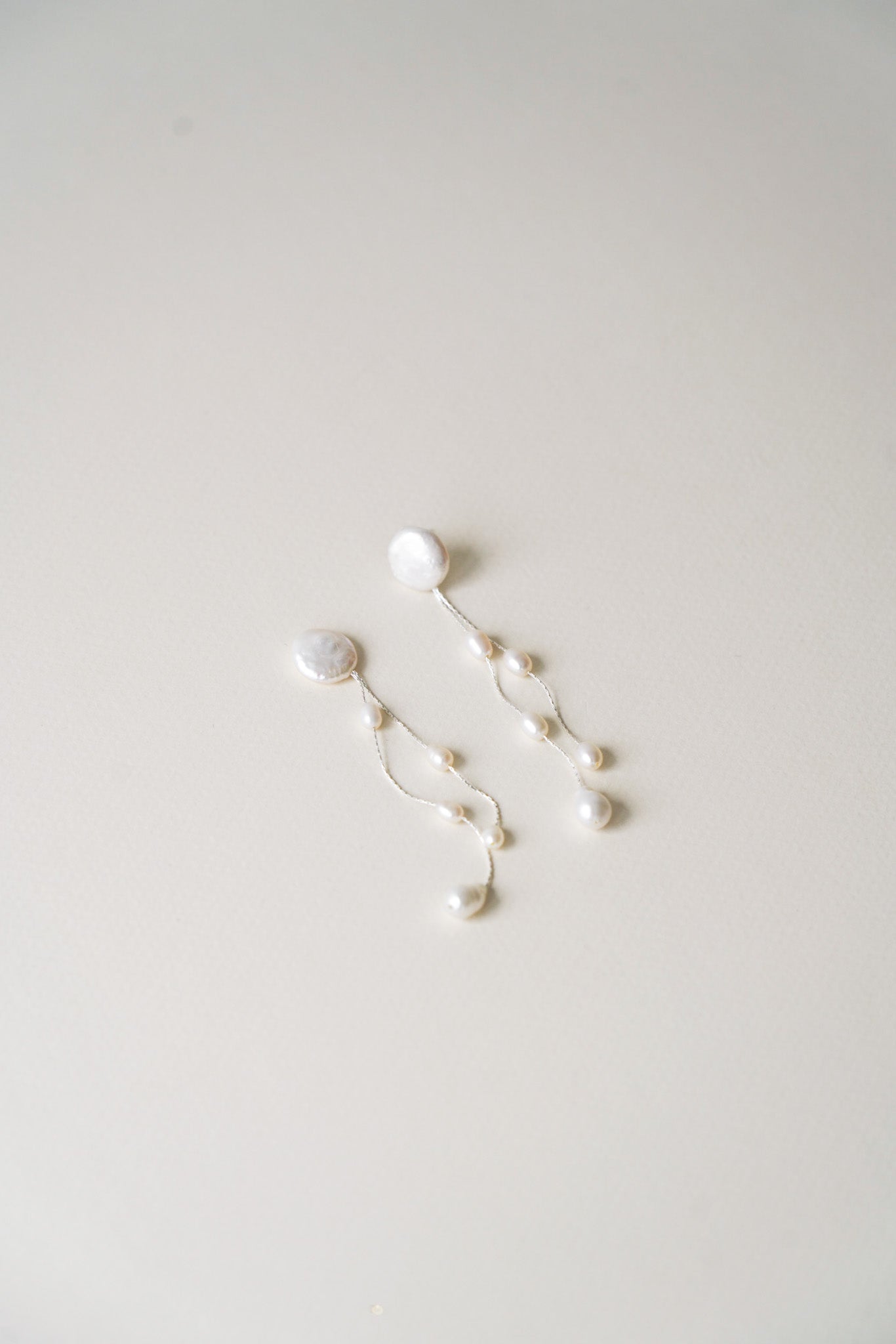 Boucles d’oreilles élégantes posées sur fond neutre, composées d’une grande perle de culture en base, suivie d’une délicate cascade de petites perles de culture naturelles. Le design fluide et raffiné évoque une silhouette élancée et lumineuse, parfaite pour une mariée en quête de douceur et d’élégance intemporelle. Un bijou de mariage chic et romantique, réalisé avec soin à la main.