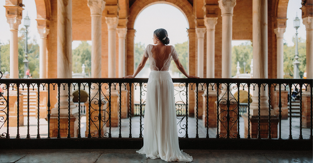 Mariée en robe plissée blanche avec grand décolleté de dos sur un balcon