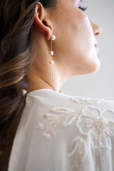 Mariée portant une paire de boucles d'oreilles pendantes avec trois perles blanches accrochées à une chaine doré 