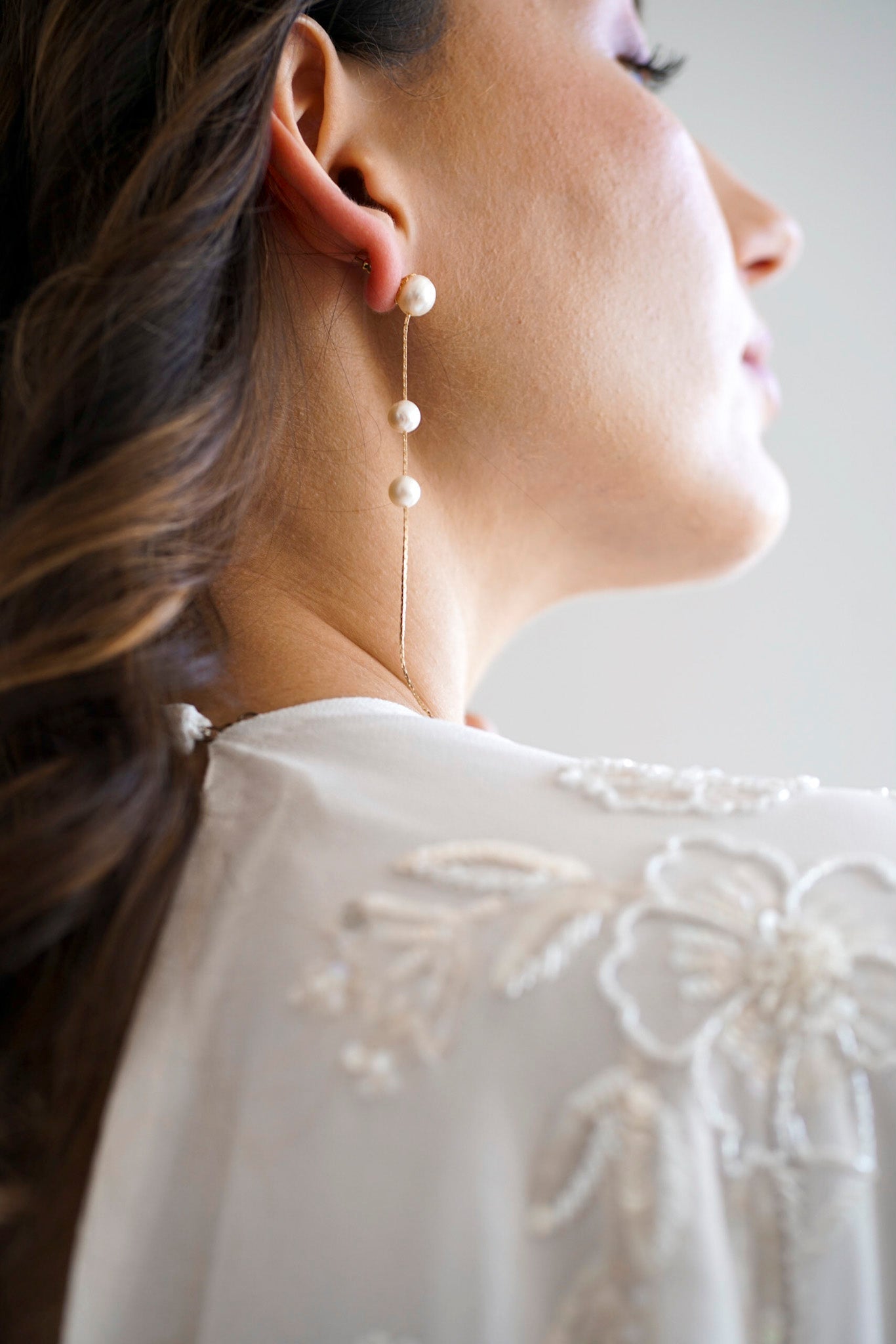 Mariée portant des boucles d'oreilles pendantes faite de trois perles naturelles de culture accrochées à une chaine en or