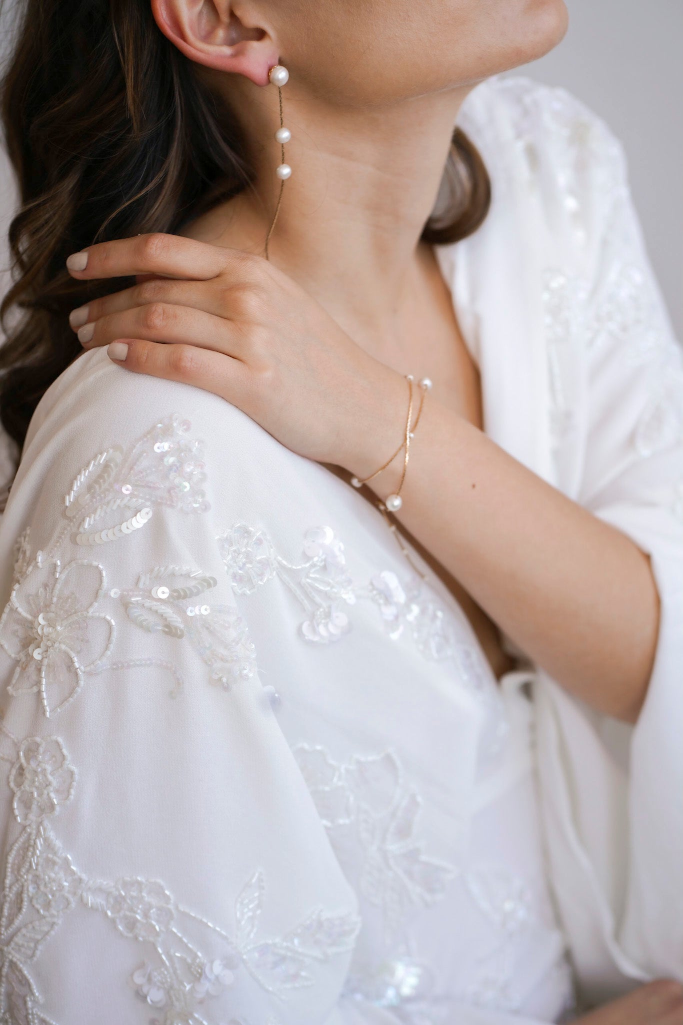 Mariée portant un un bracelet à double chaine dorées parsemées de perles blanche, et des boucles d'oreilles pendantes à chaine doré et trois perles blanches