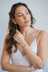 Mariée portant un bracelet, un collier de dos et des boucles d'oreilles pendantes de mariage couleur argent avec des pierres bleues
