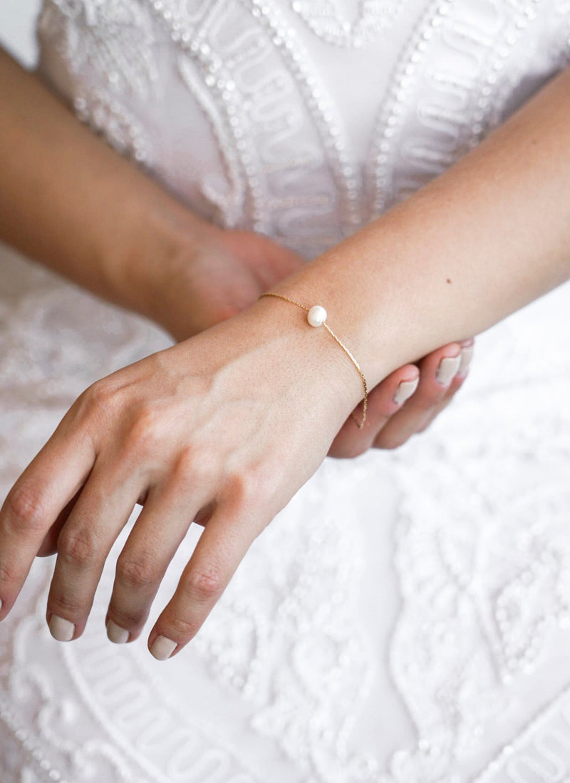 Mariée portant un bracelet fin fait d'une chaine couleur or et d'une perle ronde 
