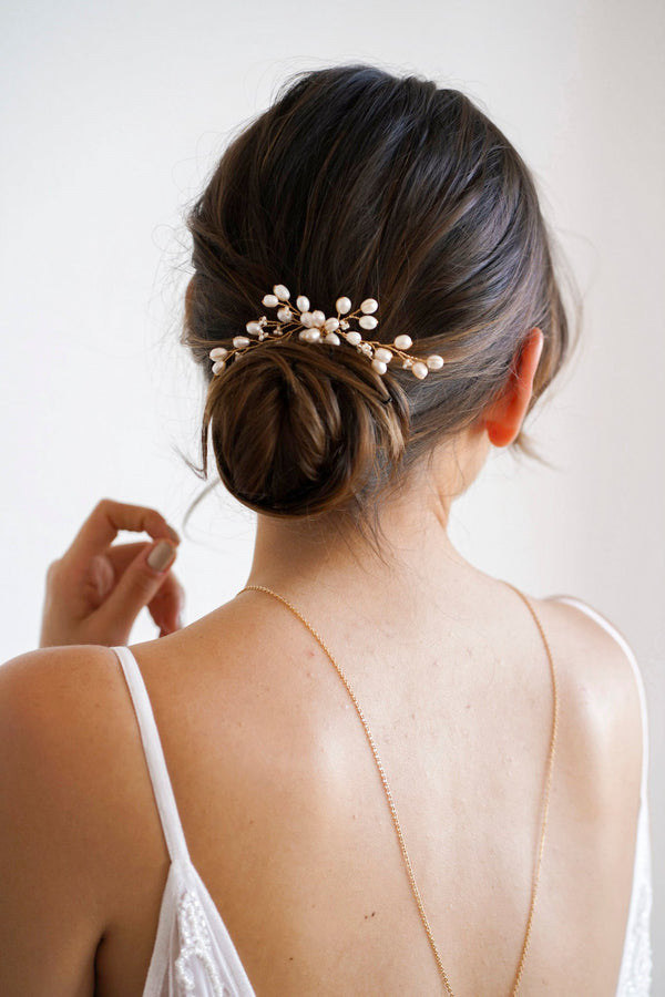 Mariée coiffée d'un chignon bohème formant un bouquet de perles relié par des fils dorés entrelacés