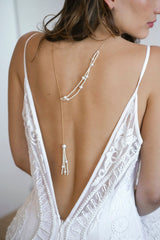 Mariée portant un collier de dos fait avec une chaine en or et une autre chaine en perles rocailles et perles naturelles de culture blanches formant un pompom au bout