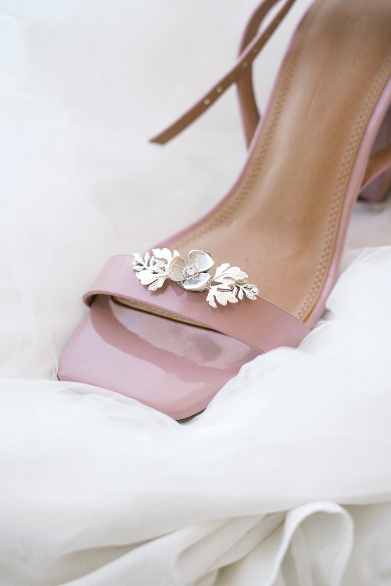 clip à chaussure argenté avec une fleur et feuillages placé sur une paire de talons rose poudré