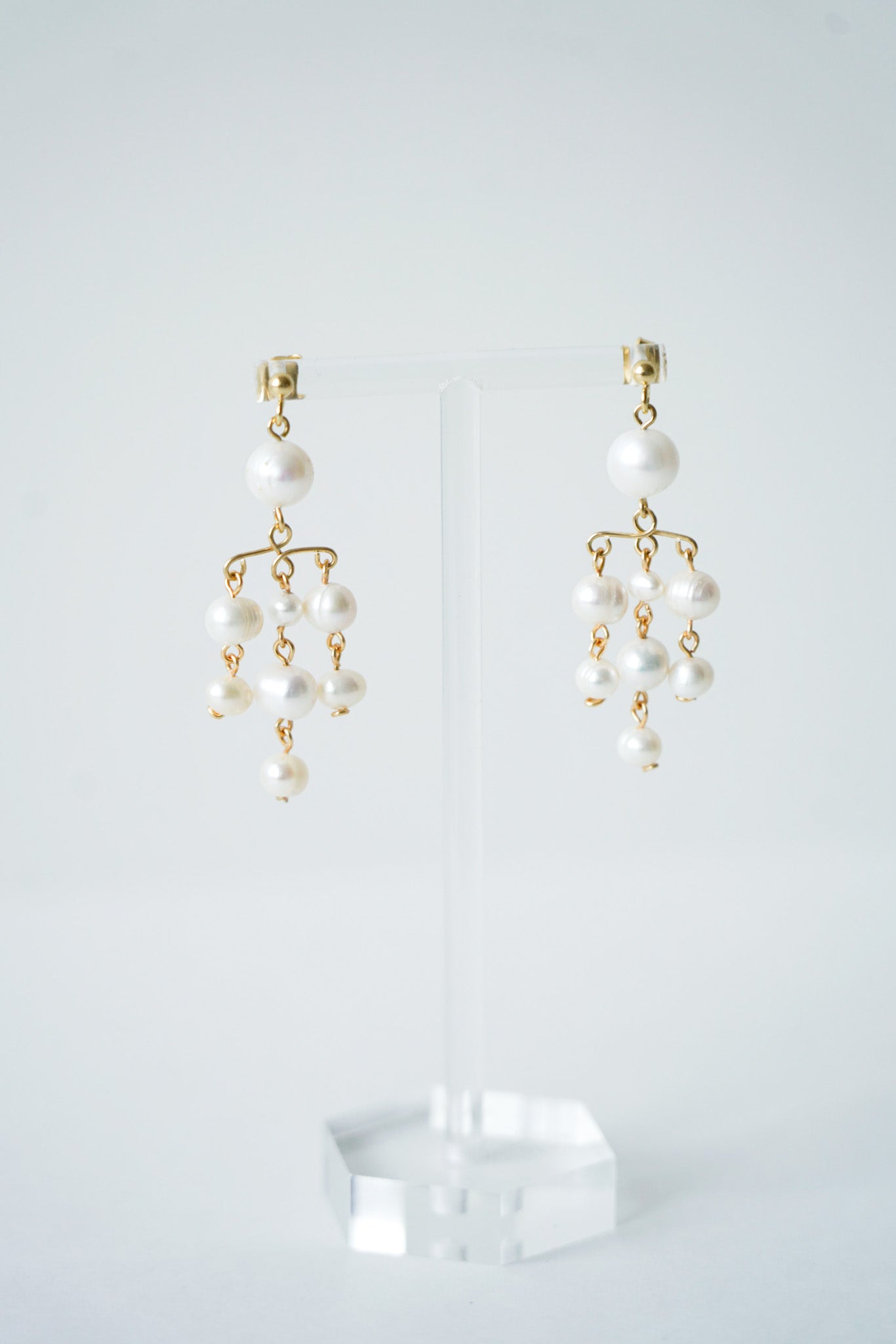 une paire de boucles d'oreilles moderne pour mariage fabriquée avec des perles naturelles rondes posé sur un portant transparent à bijoux