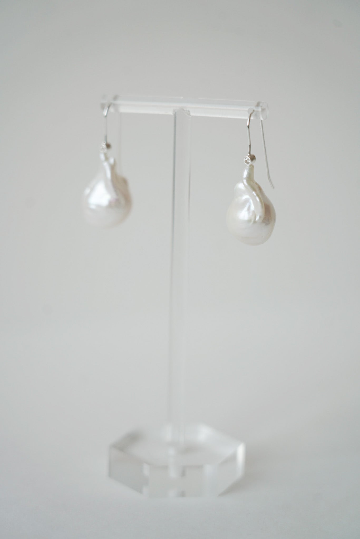 une paire de boucles d'oreilles pour mariage avec des perles naturelles irrégulière baroque et une attache argenté sur un portant à bijoux transparent