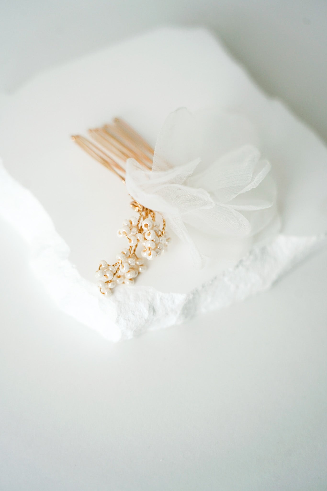 peigne pour un mariage avec des perles rocailles et du tule posé sur un pierre blanche et sur une table blanche