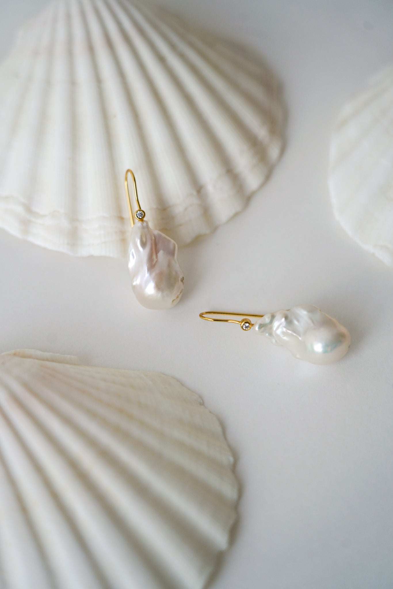 boucles d'oreilles avec une perle naturelle baroque irrégulière pour mariage et son attache dorée sur une table blanche avec des coquillages en fond