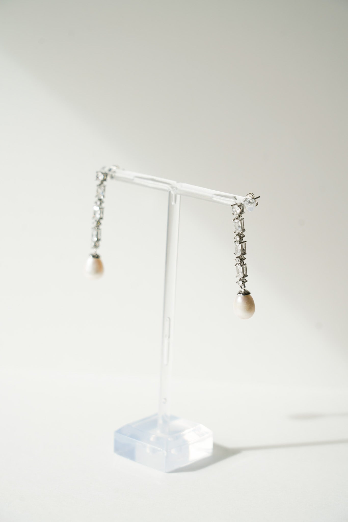 paire de boucles d'oreilles pendantes en cristal avec des perles naturelles au bout sur un portant transparent