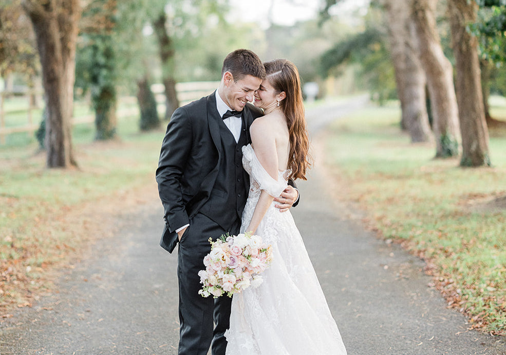 Deux jeunes mariés s'enlacent en rigolant et portant pour la femme des bijoux de mariage de l'Atelier Lilac