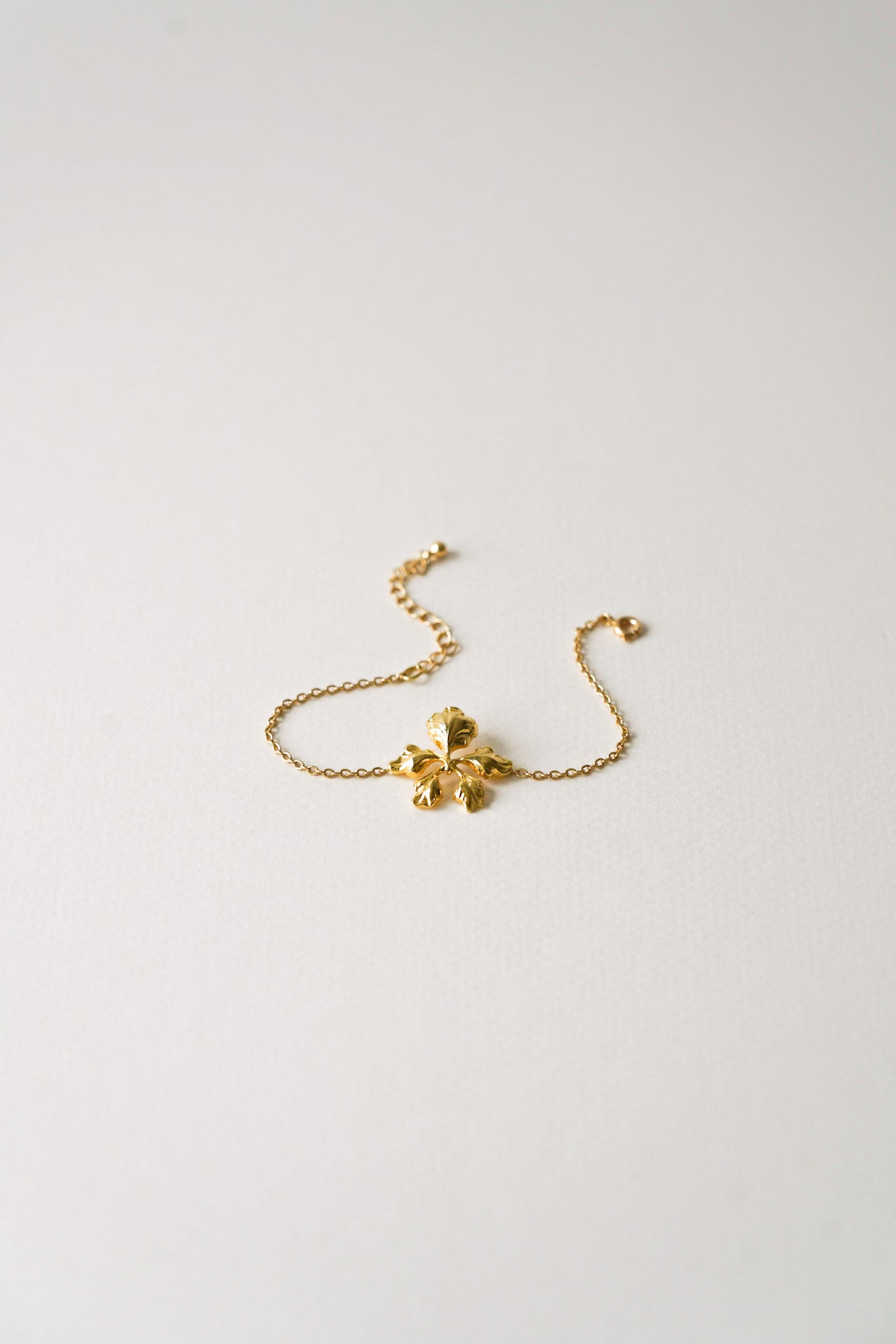 Bracelet doré délicatement posé sur fond clair, orné d’une fleur asymétrique et légèrement déstructurée, aux pétales finement courbés, apportant une touche de modernité et de poésie. Parfait pour un mariage, ce bijou allie élégance et originalité, avec une finition lumineuse et raffinée, idéale pour sublimer un poignet de mariée.