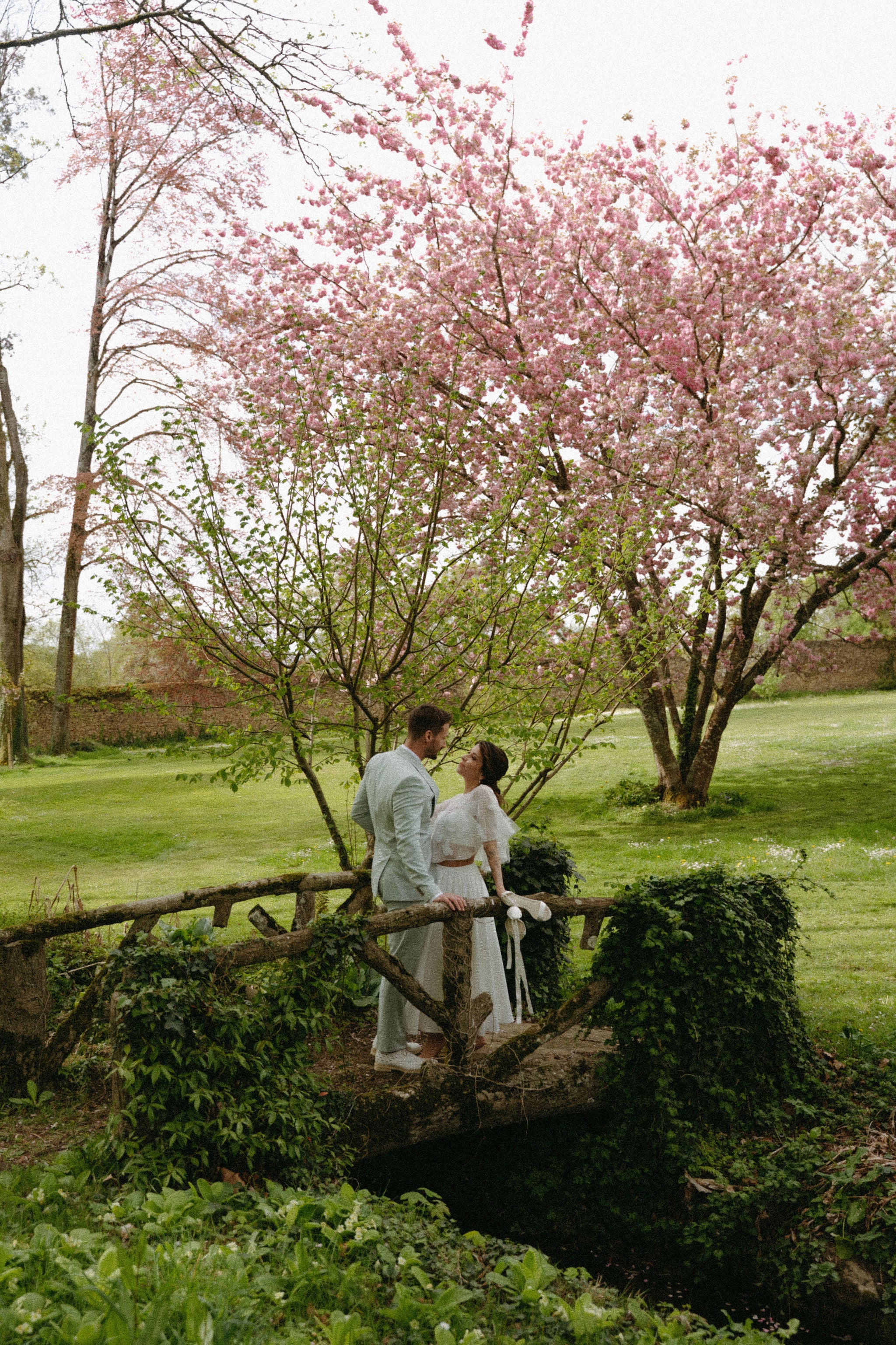 Photo de mariage de couple amoureux dans un jardin sous un arbre en fleurs, photo de mariage romantique, mariée élégante, mariage au château élégant, inspiration mariage château 
