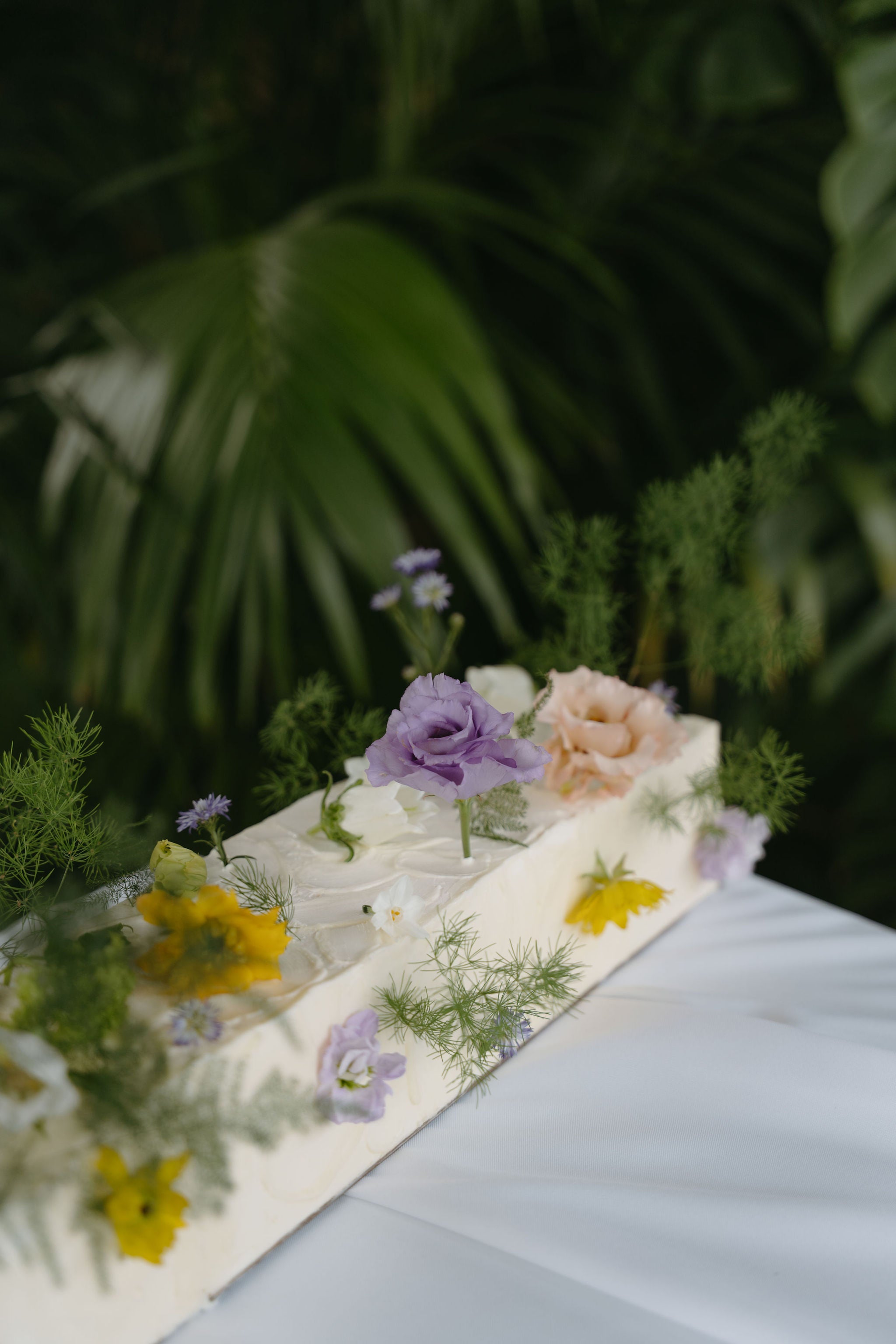 Gâteau de mariage blanc à la crème avec des fleurs posé sur une table blanche avec des feuillages, gâteau de mariage, wedding cake, cake design 