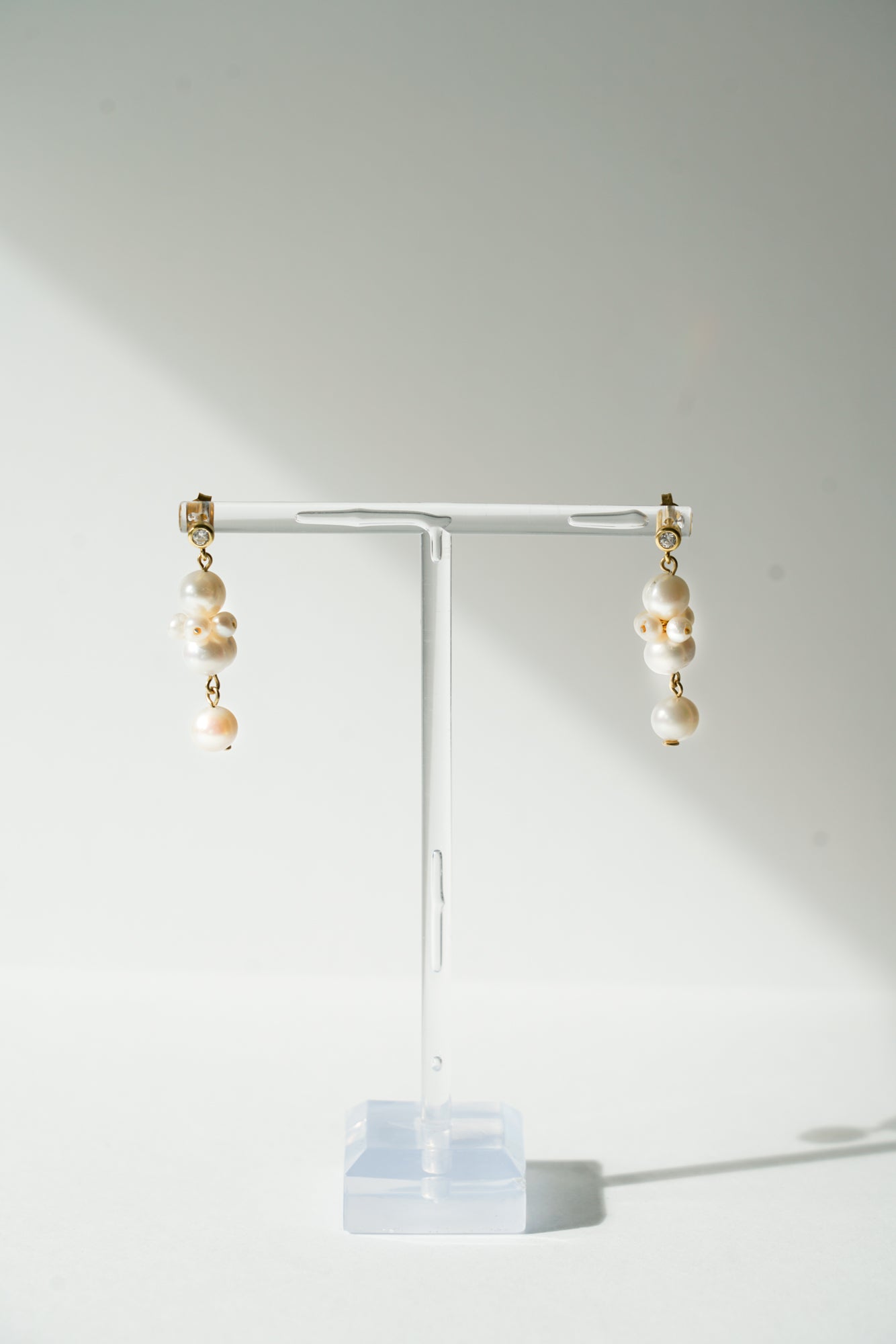 paire de petites boucles d'oreilles en perles naturelles en forme ronde unique sur un portant transparent à bijoux