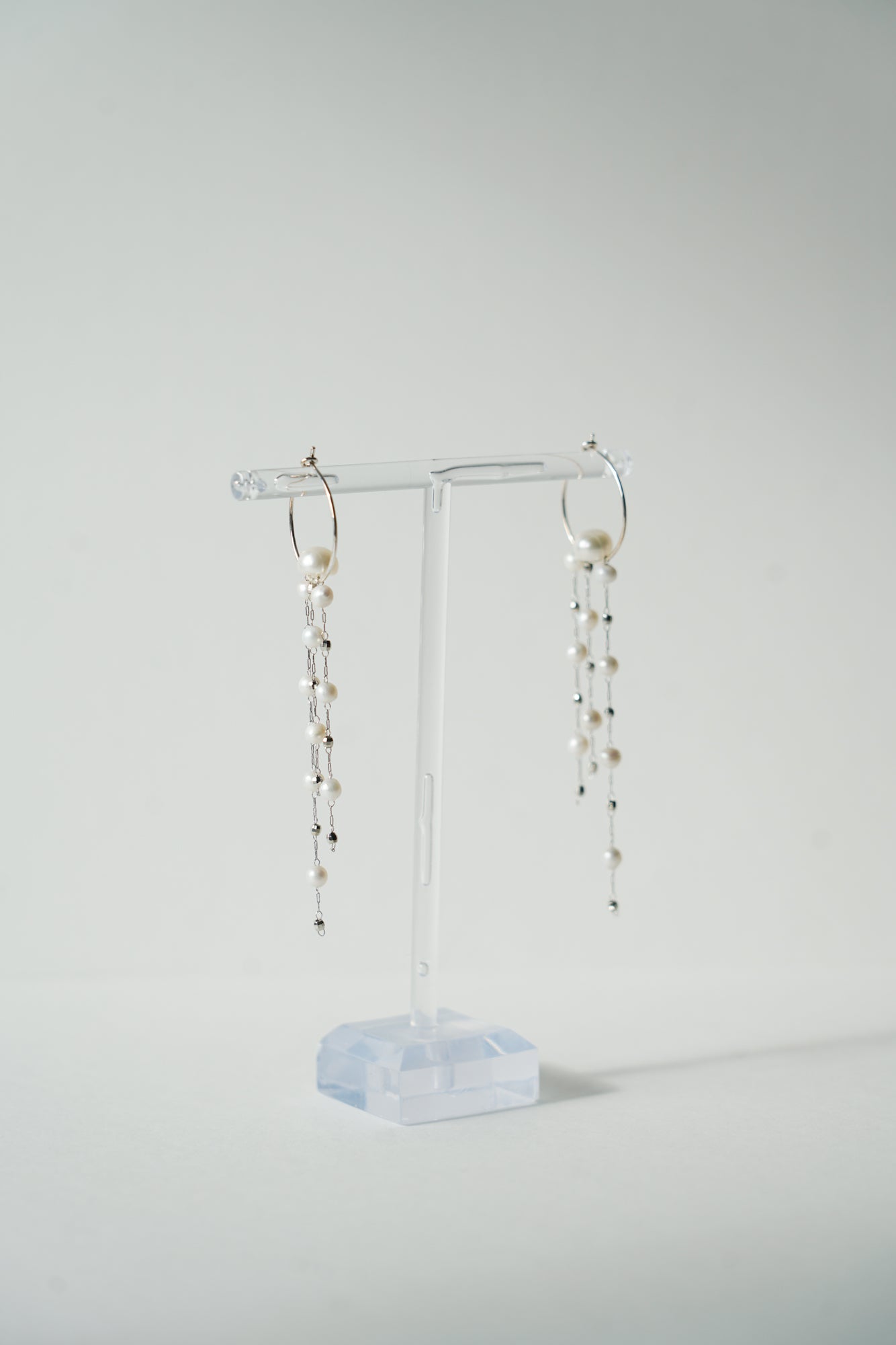 boucles d'oreilles pour mariée sur un portant à bijoux transparent fait des des chaines perles naturelles