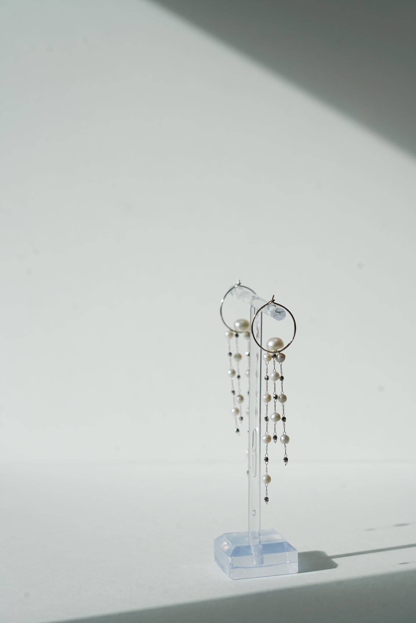 boucles d'oreilles pour mariée positionné sur le côté sur un portant à bijoux transparent fait des des chaines perles naturelles