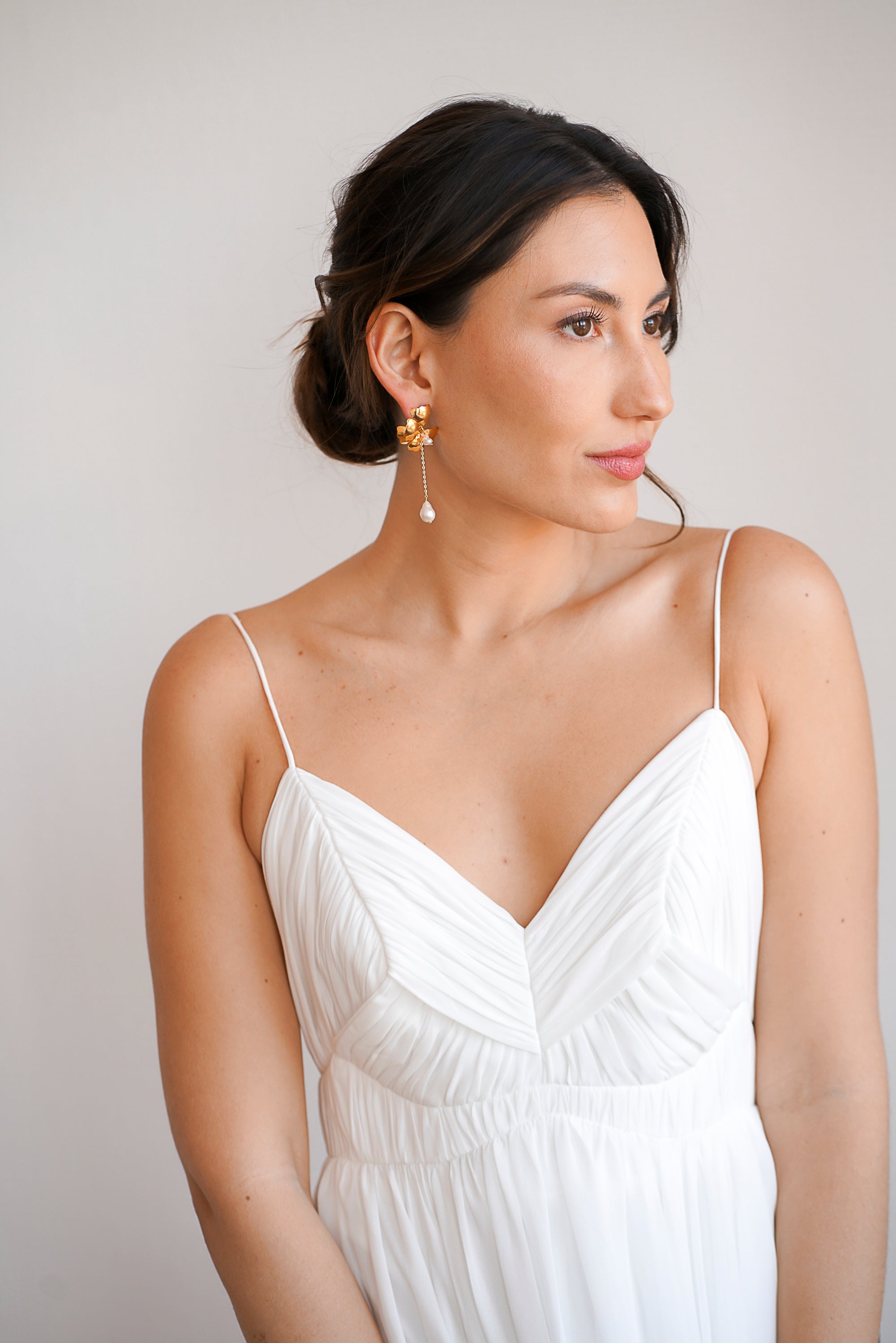 Boucles d'oreilles de mariage aver fleur en bronze plaqué or ornée de perles naturelles portées par une femme en robe de mariée