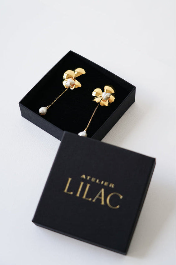 boucles d'oreilles mariage florale avec une perle naturelle dans une boite à bijoux noir avec le logo de la marque atelier lilac 