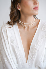Mariée portant un collier à trois branches fait de perles rocailles et de perles naturelles avec des boucles d'oreilles fleurs dorées