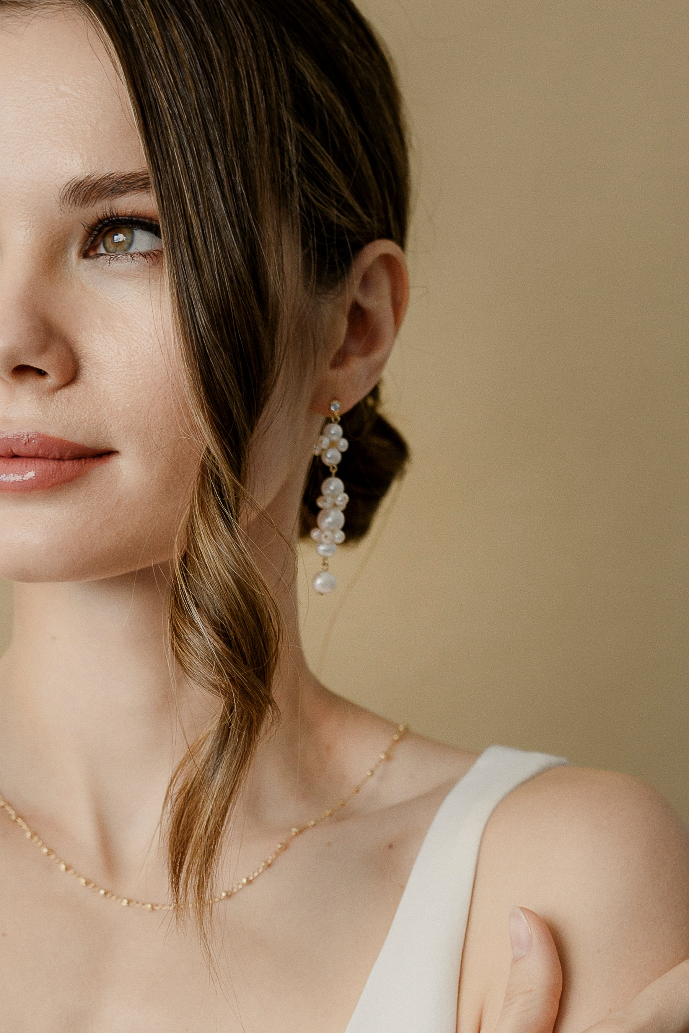 Photo qui montre une partie du visage d'une femme regardant sur le côté mettant en avant ses bijoux de mariage notamment ses boucles d'oreilles de cérémonie et son collier de dos 