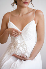 Mariée tenant dans ses mains un sac de mariée blanc fait de perles et d'un tissu en satin