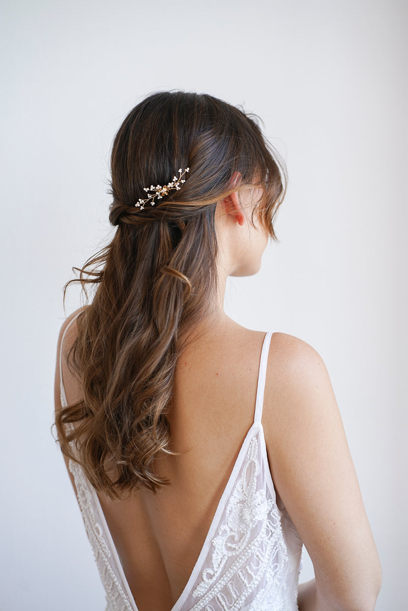 Mariée avec de belles boucles bohèmes portant un pic à cheveux de mariage très fin de couleur doré avec des fleurs blanches