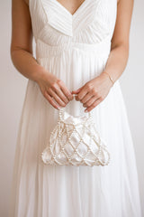 Mariée de face tenant un sac de mariée en satin blanc et en perles blanches